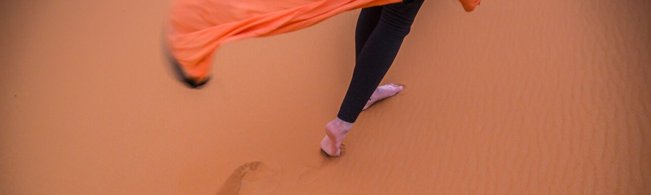 Feet walking on desert sand with flowing tunic